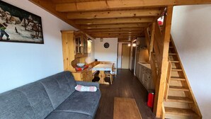 A cozy room with a wooden ceiling, a gray sofa, a dining table with chairs, and a staircase. - Les Saisies - Spacious 3 Rooms Mezzanine 2 Bathrooms for 8 Pers. (Les Saisies)