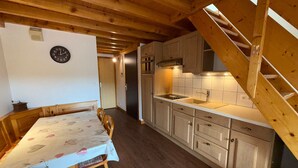 A wooden interior with a dining table, chairs, a clock, and a kitchen area with cabinets and a sink. - Les Saisies - Spacious 3 Rooms Mezzanine 2 Bathrooms for 8 Pers. (Les Saisies)