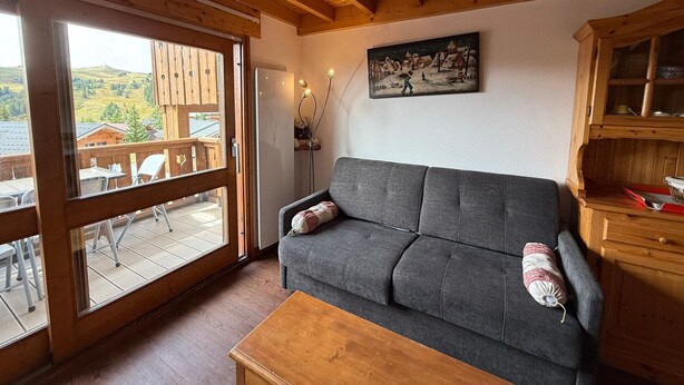 A cozy living room with a grey sofa, wooden coffee table, and a painting of a village scene. - Les Saisies - Spacious 3 Rooms Mezzanine 2 Bathrooms for 8 Pers. (Les Saisies)