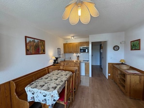 A compact kitchen with wooden cabinets, a dining table with a patterned tablecloth, and a hanging light fixture.