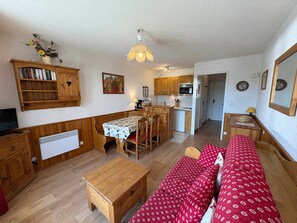 A cozy living room with a sofa, a dining table, and a kitchen area with wooden cabinets and a microwave.