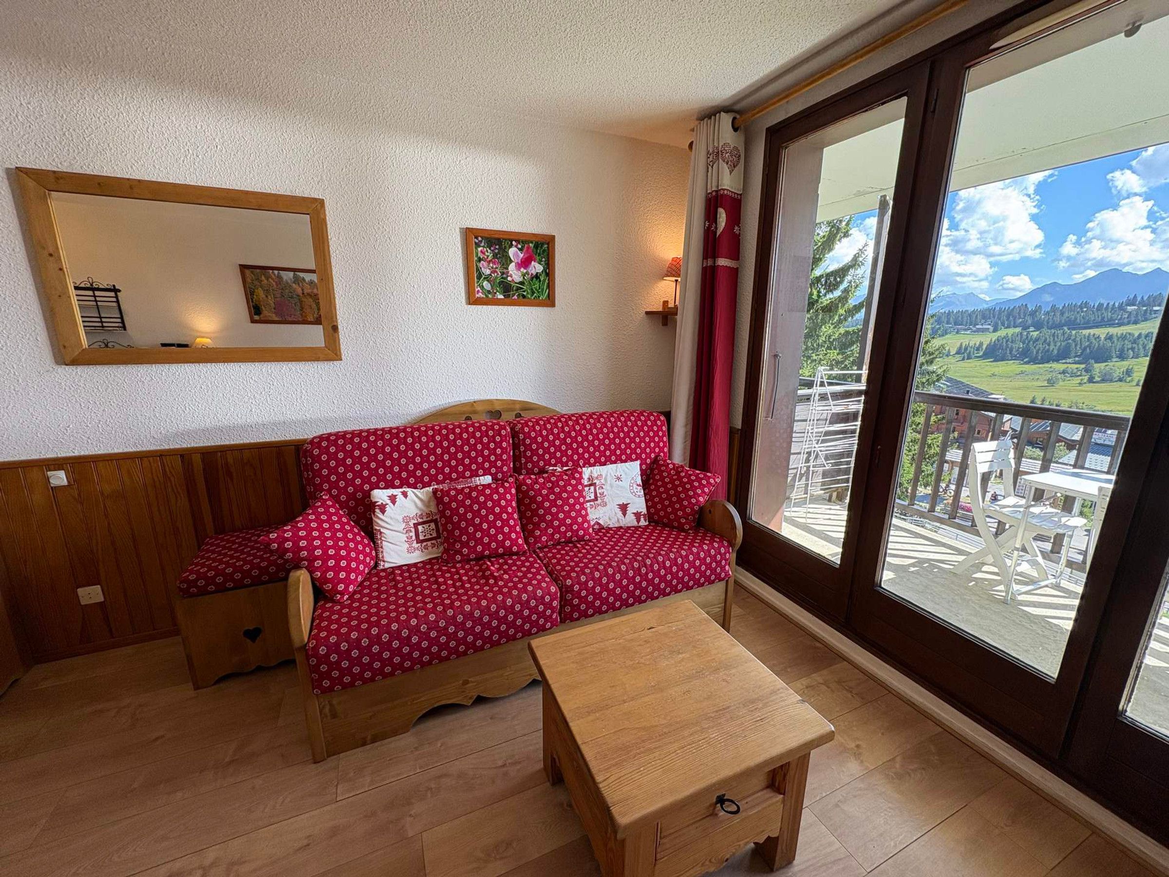 Quarto com sofá de madeira, uma pequena mesa de madeira e uma janela grande com vista para uma varanda e montanhas.