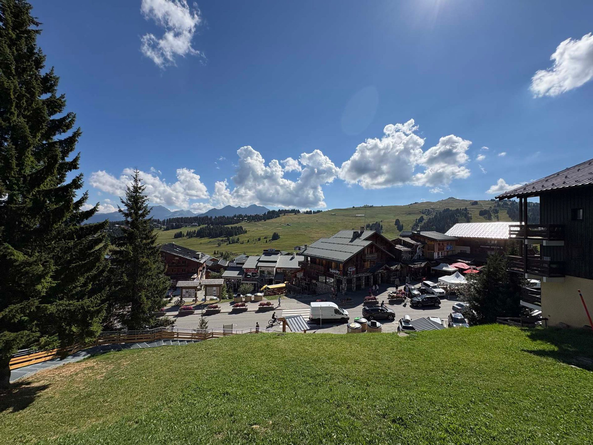 A mountain village with traditional wooden buildings, a parking area, and a view of the surrounding hills.