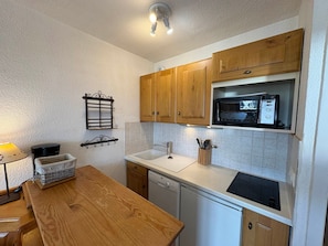 A compact kitchen with wooden cabinets, a microwave, a dishwasher, and a small dining area with a table and chairs.