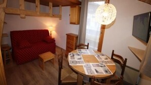 Une pièce chaleureuse avec un plafond en bois, un canapé rouge, une table à manger avec un set de table et un luminaire suspendu.