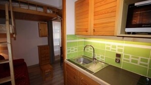 Une cuisine compacte avec des meubles en bois, un crédence carrelée de couleur verte et un micro-ondes encastré.