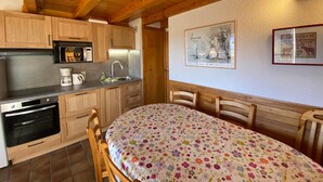 Une cuisine avec des meubles de rangement en bois, un four encastré et un coin repas agrémenté d’une nappe à motifs floraux.
