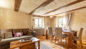 A cozy living room with a wooden coffee table, a sofa with decorative pillows, and a dining area with a wooden table and chairs. - CHARMING HOUSE IN THE COUNTRY  (Sommerau)
