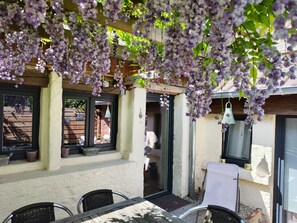 Un patio al aire libre con una mesa y sillas, un colgante de luz y flores moradas.