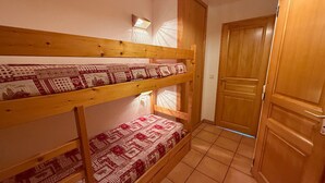 A bunk bed room with patterned bedding, a wooden door, and a tiled floor. - Cozy studio in Les Saisies, 5 pers, south balcony (Les Saisies)