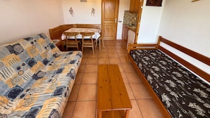 A compact room with a wooden bench, a sofa, a dining table with chairs, and a kitchenette. - Cozy studio in Les Saisies, 5 pers, south balcony (Les Saisies)