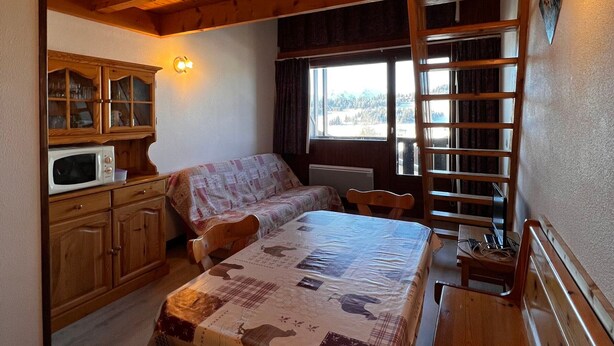 Une chambre confortable dans un chalet, avec un lit, une armoire en bois dotée de portes en verre, un four à micro-ondes et une fenêtre donnant sur la forêt.