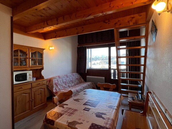 A cozy cabin room with a bed, a wooden cabinet with glass doors, a microwave, and a window with a view of trees.