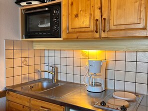 A kitchen with wooden cabinets, a microwave, a coffee maker, and a sink.