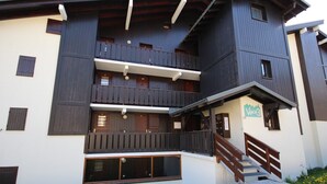 Un immeuble à plusieurs étages doté de balcons en bois, d’un escalier menant à l’entrée et d’une enseigne indiquant « Village3 ».