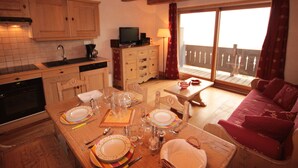 A cozy living area with a dining table set for four, wooden cabinets, a television, and a balcony with a view. - Cozy apartment in Les Saisies - 4/6 pers, 38m², south, balcony (Hauteluce)