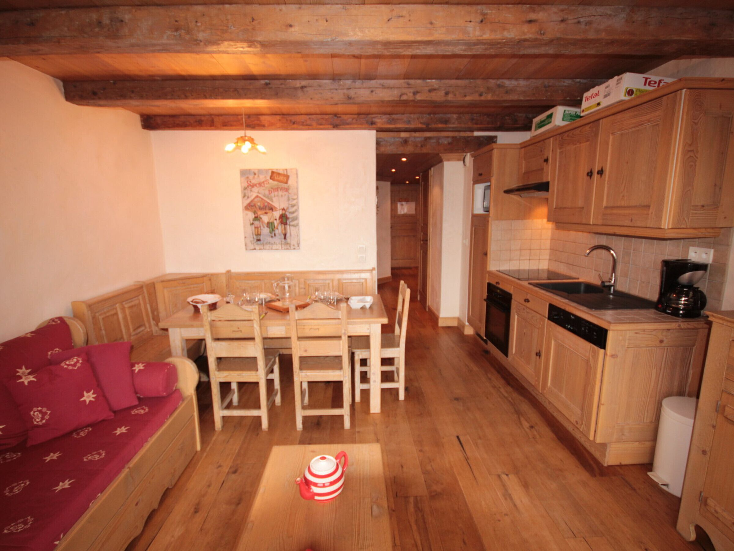 A cozy kitchen with wooden cabinets, a dining table set for four, and a red sofa in the living area.