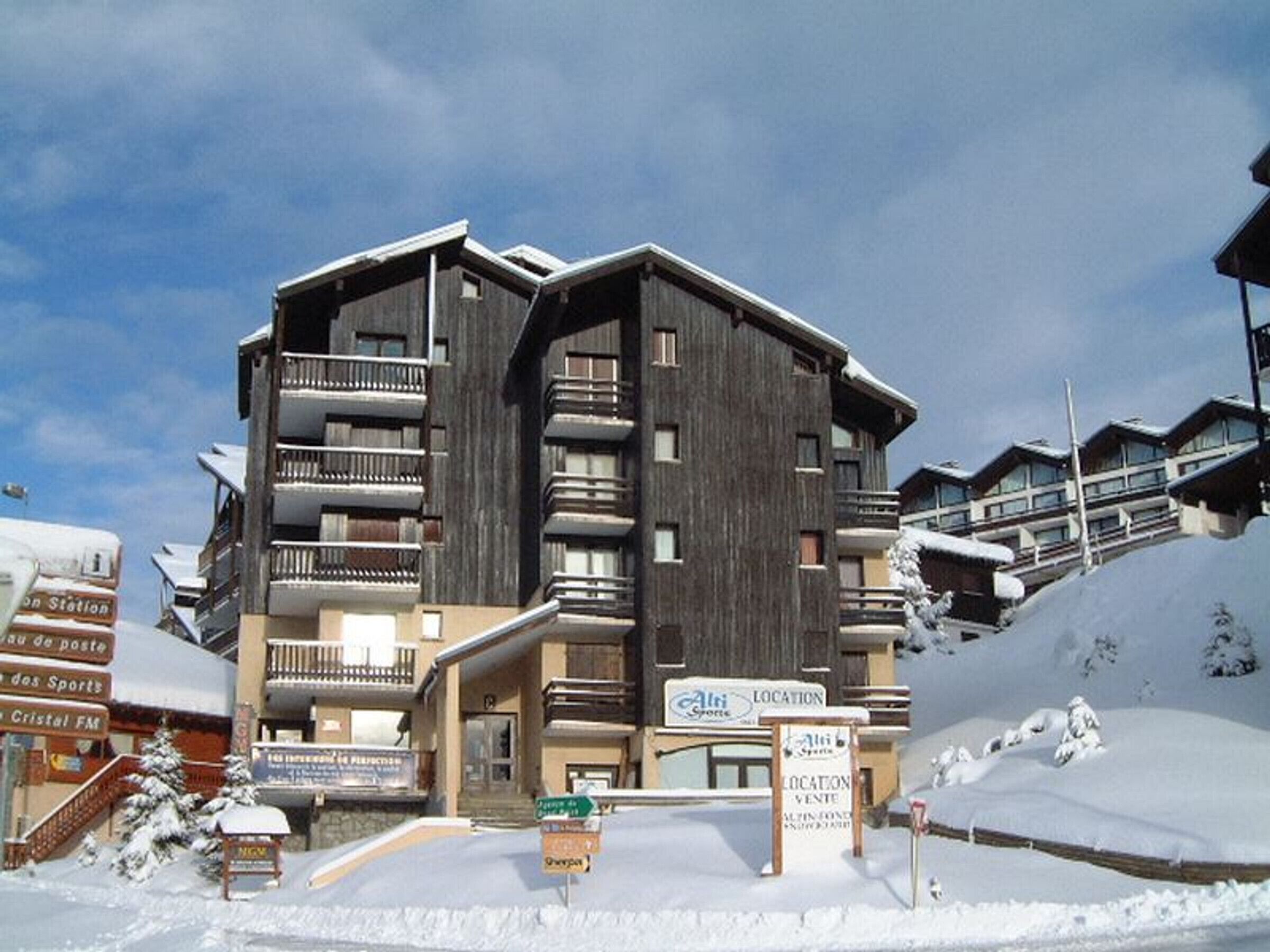 A multi-story building with balconies, a ski slope in the background, and signage indicating a location for ski rentals.