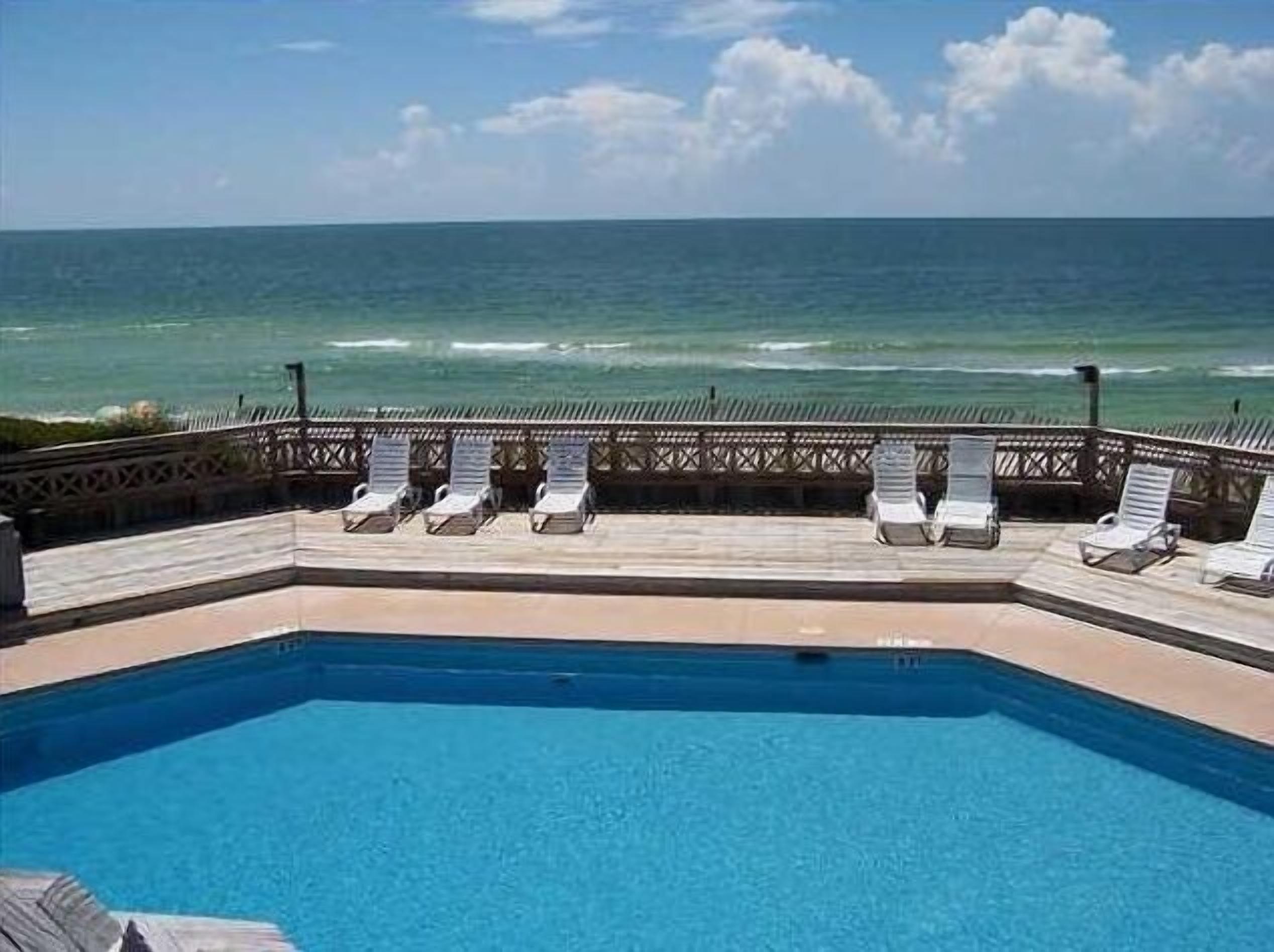 A pool with lounge chairs facing the ocean.
