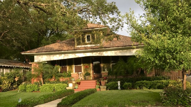A two-story house with a front porch, surrounded by well-maintained lawns and various potted plants. - Industrial chic guesthouse (Tampa)