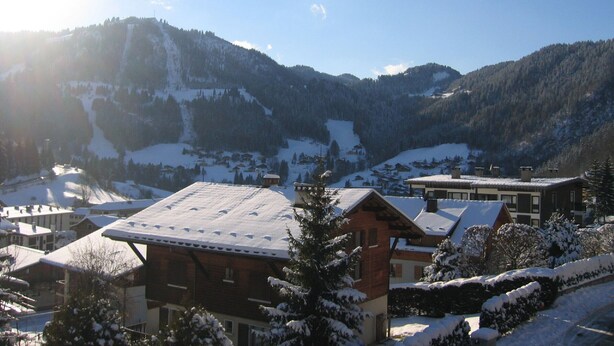 A snow-covered mountain village with chalet-style buildings, a ski slope in the background, and a clear sky. - Studio for 4 people with garage, near village and lifts (La Clusaz)