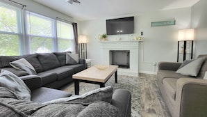 A modern living room with a fireplace, a large TV, and two couches. - RIVERVIEW VILLA AT OCEAN BEACH: 5 QUEEN BEDS (New London)