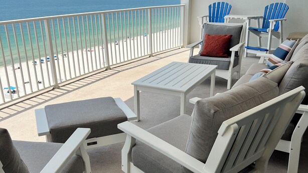 Een balkon met wit meubilair, waaronder stoelen en een tafel, met uitzicht op een strand.
