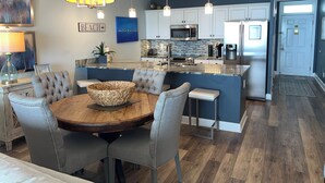 Een moderne keuken met een centraal kookeiland, roestvrijstalen apparatuur en een eethoek met een houten tafel en gestoffeerde stoelen.