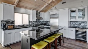 Een moderne keuken met witte kasten, een groot eiland met barkrukken, roestvrijstalen apparatuur en een houten plafond.