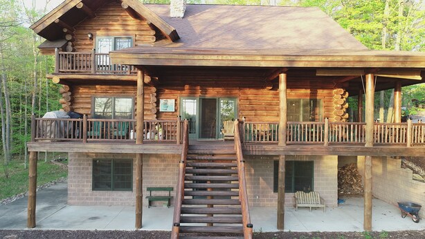 A log cabin with a balcony, a staircase, and a front door.