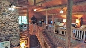 A rustic cabin interior with a stone wall, wooden beams, and a staircase leading to a loft area.