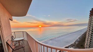 Ein Balkon mit Blick auf den Sonnenuntergang über dem Meer, inklusive Tisch und Stühlen.
