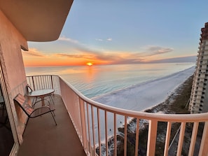 Un balcon avec vue sur le coucher de soleil sur lâocĂ©an, une table et des chaises.