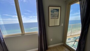 Ein Zimmer mit großem Fenster zum Meer, einem gerahmten Bild an der Wand und einem Balkon mit Blick auf den Strand.