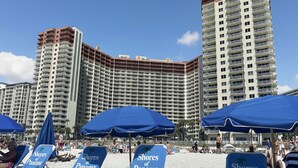 Ein Strand mit Liegestühlen, beschriftet mit 'Shores of Panama', und ein Hochhaus im Hintergrund.