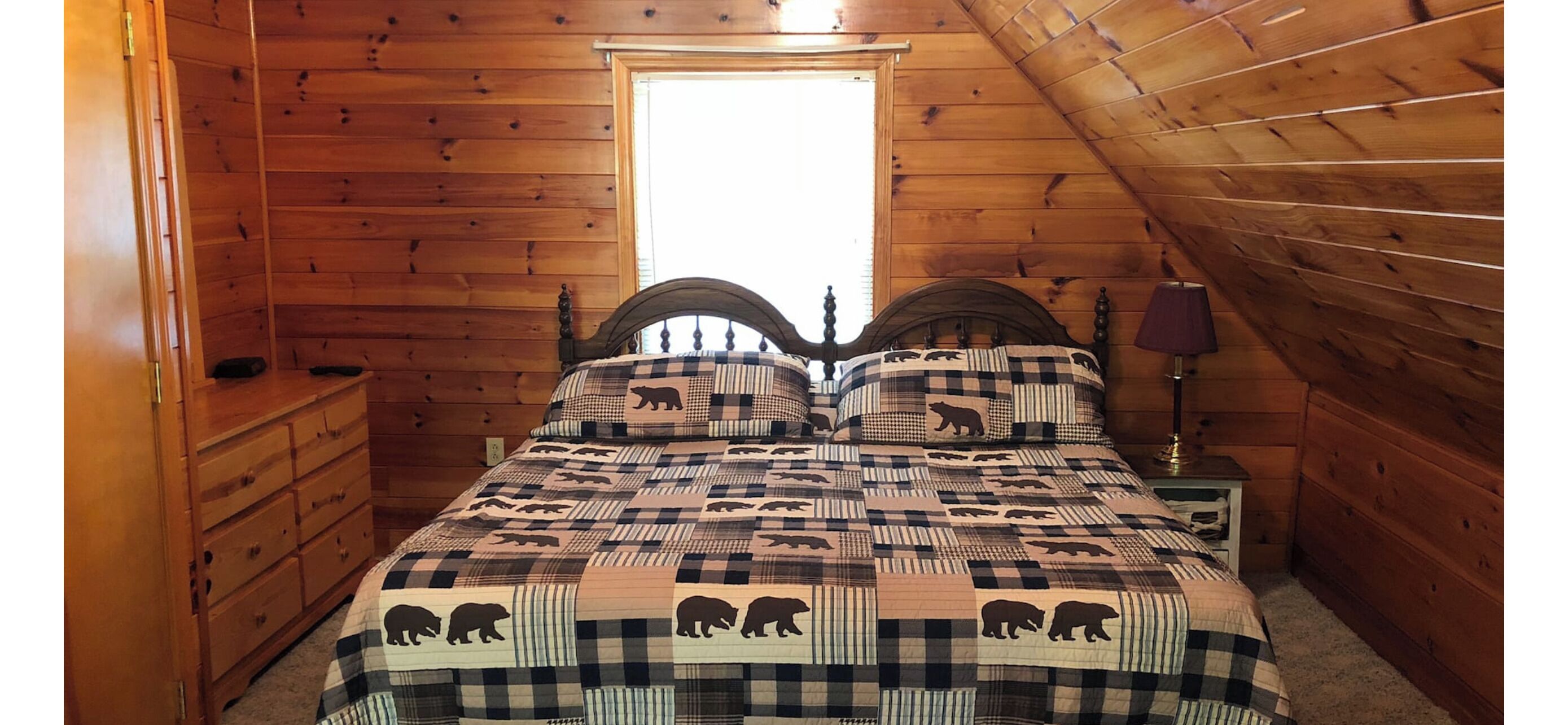 A wooden cabin bedroom with a bed, a nightstand, and a dresser.