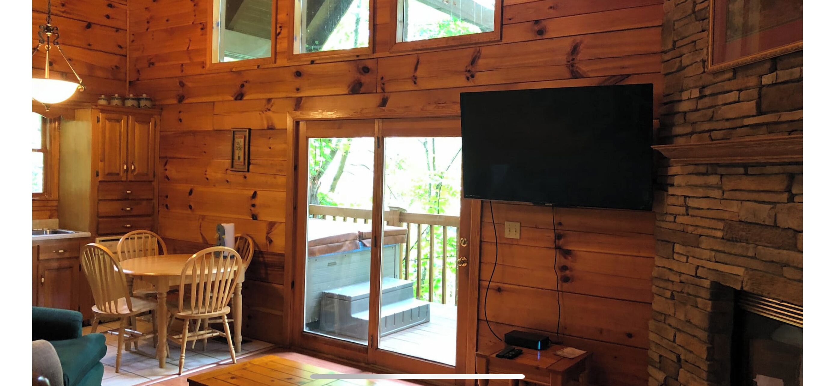 A wooden cabin interior with a dining area, a fireplace, and a television mounted on the wall.