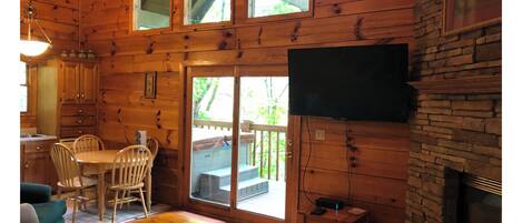 A wooden cabin interior with a dining area, a fireplace, and a television mounted on the wall.
