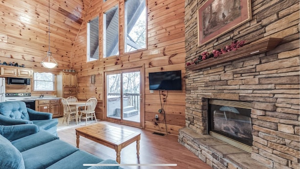 A log cabin interior with a living room, dining area, kitchen, stone fireplace, and large windows. - *Winter Special* 2 bed 2 bath 10 min PF Private (Sevier County)