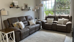 A living room with two brown leather sofas, a white side table, and a large window with a view of greenery.