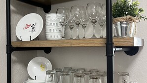 A wooden shelf unit with multiple storage options including glassware, plates, and a small potted plant.