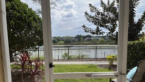 A view through a glass door of a backyard with a lawn, a small pond, and a fence.