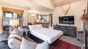 Une chambre d’hôtel moderne dotée d’un grand lit, d’un canapé, d’une télévision, d’un coin cuisine et d’une tête de cerf fixée au mur.