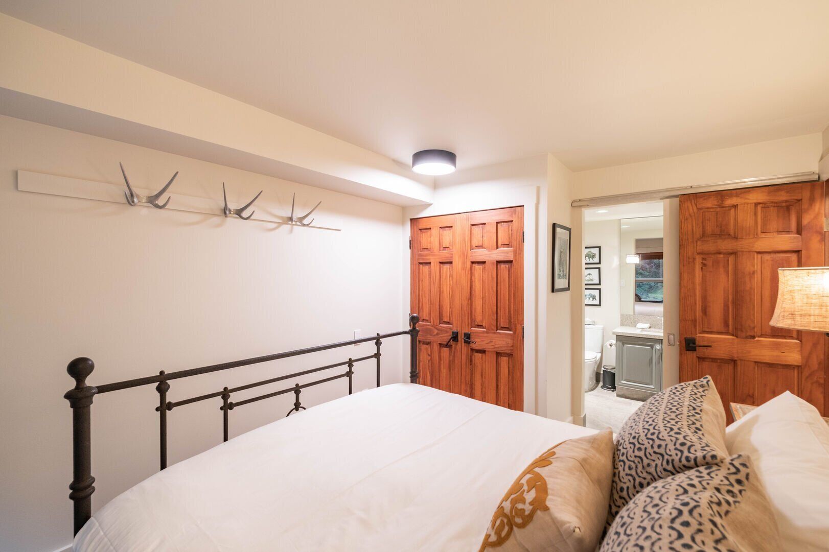 Une chambre à coucher avec un lit, une armoire en bois et une salle de bain visible à travers une porte ouverte.