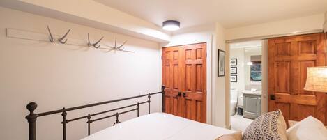 Une chambre à coucher avec un lit, une armoire en bois et une salle de bain visible à travers une porte ouverte.