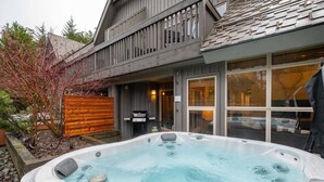 Un bain à remous dans un jardin, avec une terrasse en bois et un barbecue.