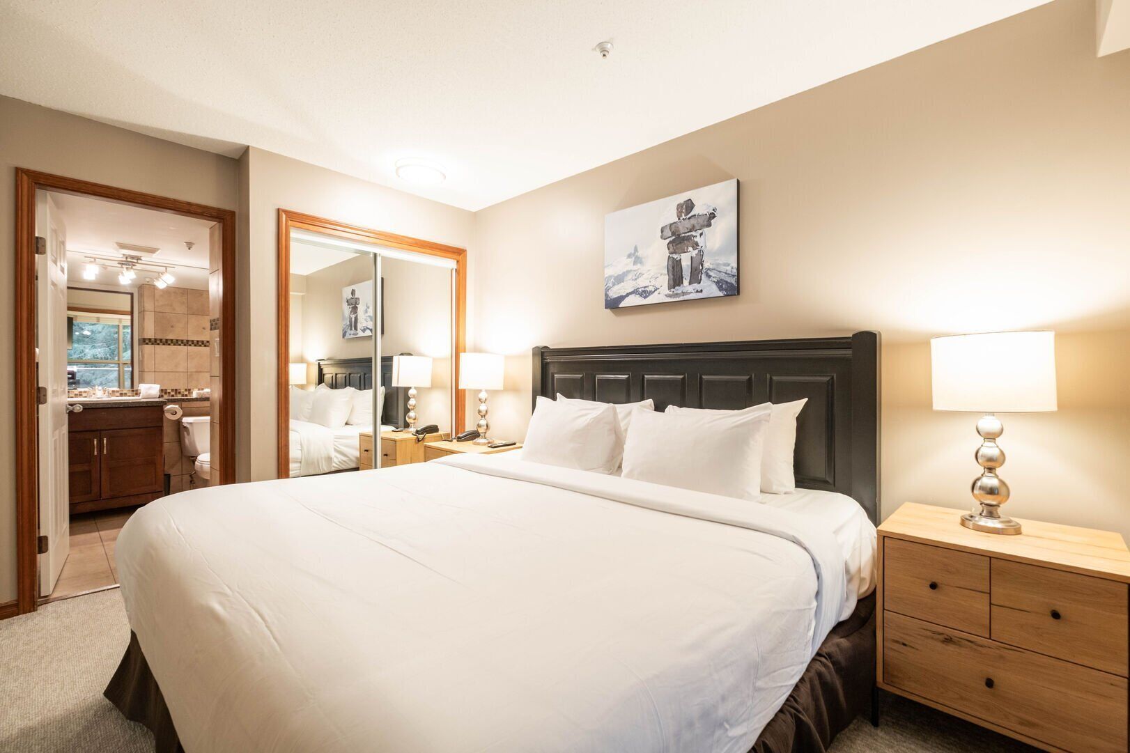 Habitación de hotel con una cama grande, mesitas de noche, un espejo y un cuadro en la pared.