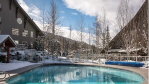 Area piscina con un edificio sullo sfondo, circondata da alberi innevati e cielo sereno.