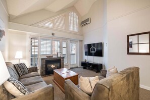 A living room with a fireplace, a television, and a large window with blinds.