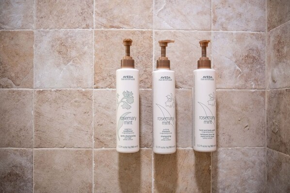 Three bottles of Aveda Rosemary Mint shampoo and conditioner on a tiled wall.